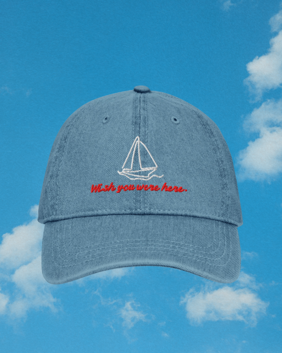 Maritimer Wish You Were Here embroidered denim cap against blue summer sky